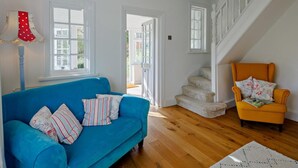 A room with a blue sofa, a yellow armchair, wooden flooring, white walls, and a staircase. - 6 Bed in Abergele (oc-91054) (Llanddulas)