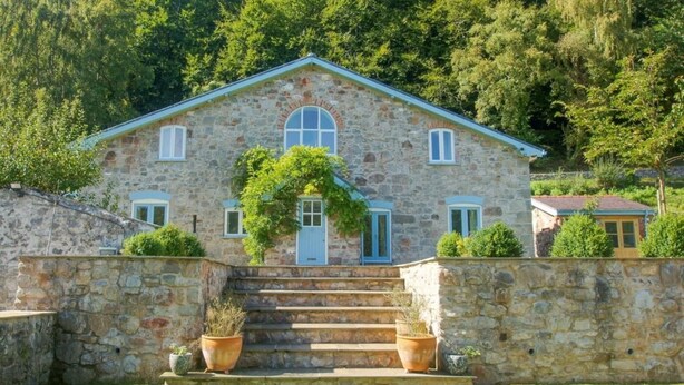 A stone house with a central entrance, a staircase leading up to the door, and a surrounding stone wall. - 6 Bed in Abergele (oc-91054) (Llanddulas)