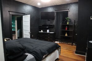 A bedroom with a bed, a TV, a wardrobe, and a shelf with a plant. - The Brown Mill Residence. (Atlanta)