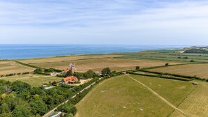 A rural landscape with a windmill, open fields, and a body of water. - 4 Bed in Holt (oc-91228) (Weybourne)