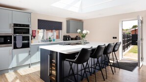A modern kitchen with a central island, bar stools, a built-in oven, and a skylight. - 4 Bed in Holt (oc-91228) (Weybourne)