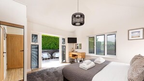 A bedroom with a bed, a desk, and a view of a green garden. - 4 Bed in Holt (oc-91228) (Weybourne)