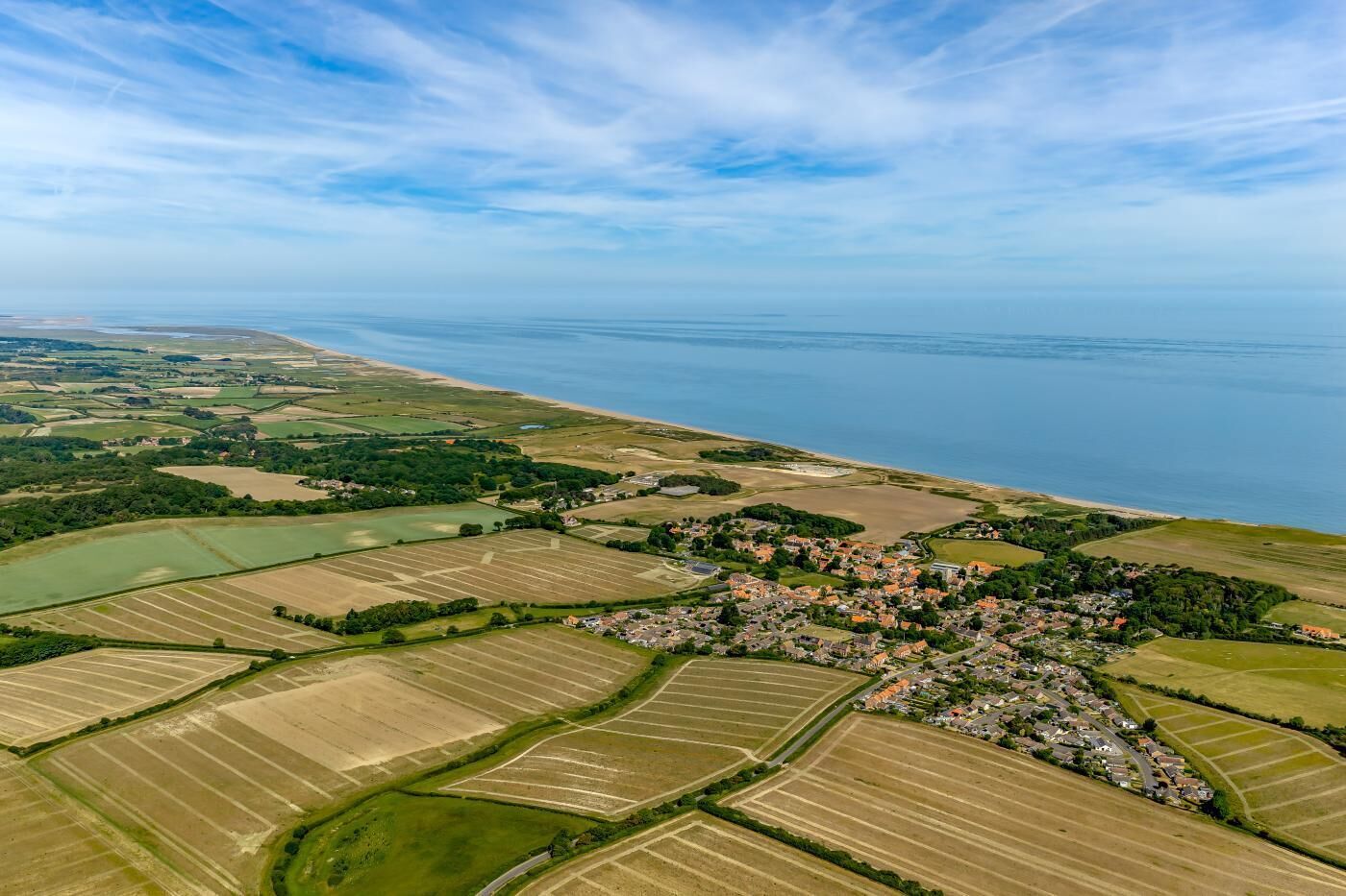 Vista aérea de un pueblo costero con campos, una playa y un pequeño poblado.