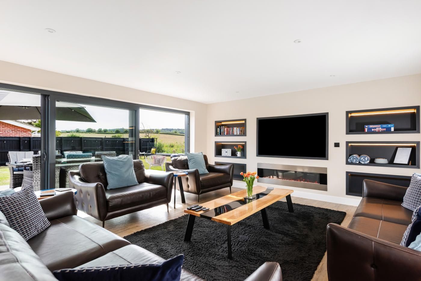 A modern living room with leather sofas, a flat-screen TV, and a fireplace.