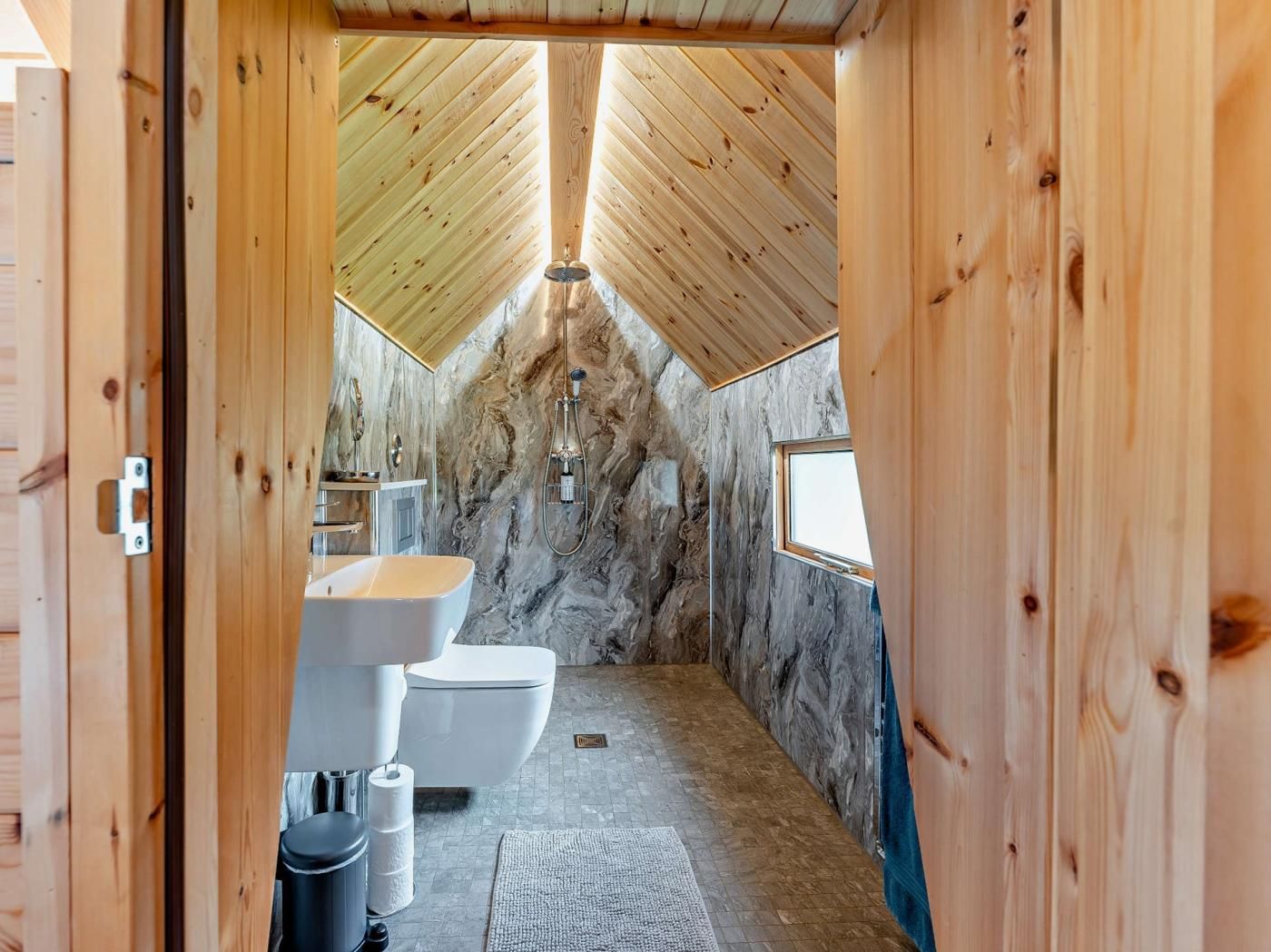 Une petite salle de bain avec un plafond en bois, un mur en marbre, un lavabo, des toilettes et une douche.
