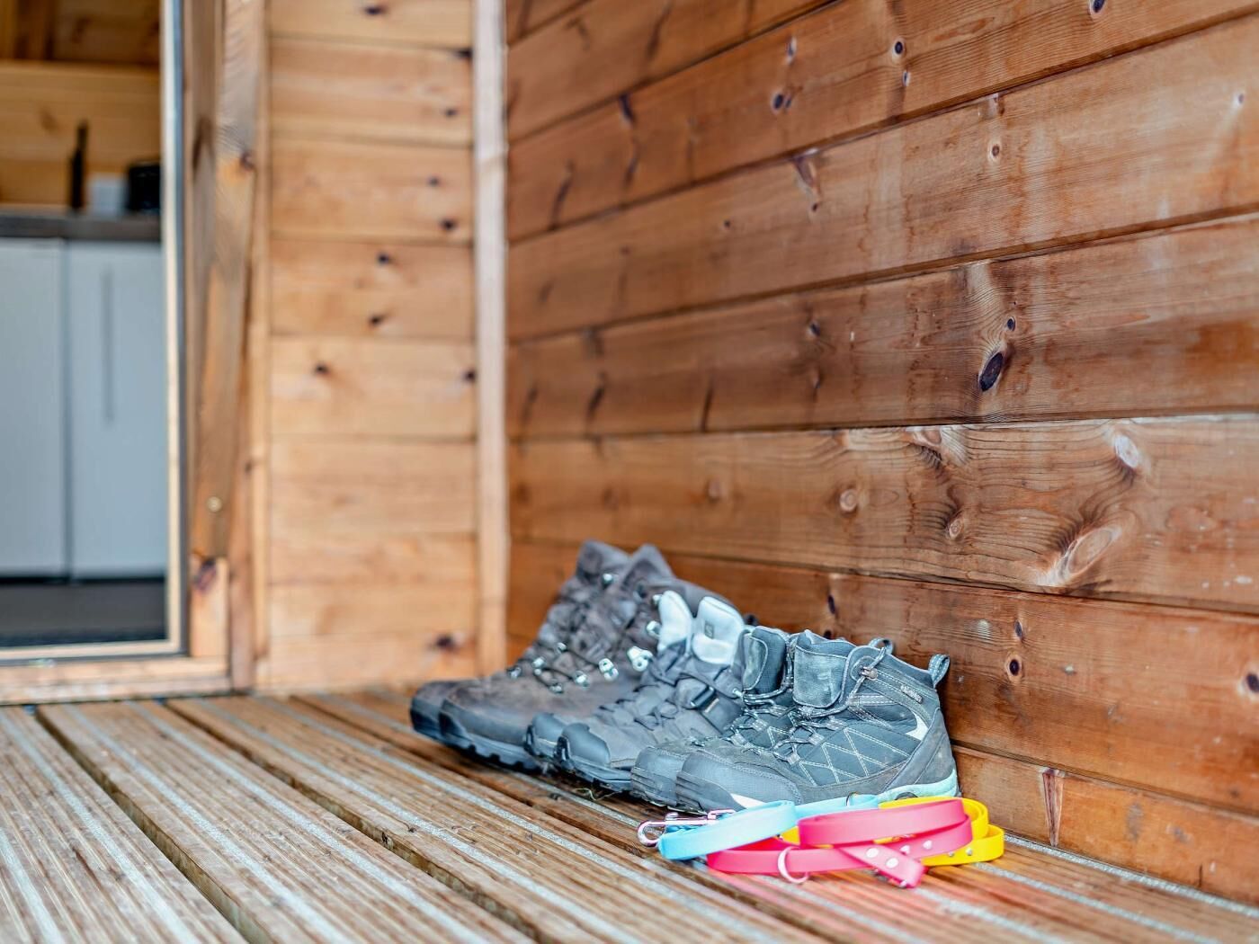 L’intérieur d’un chalet en bois, avec une paire de chaussures de randonnée et des sangles colorées posées sur le sol.