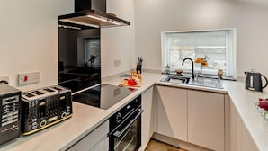 A modern kitchen with a black range hood, a built-in oven, a toaster, and a window with blinds. - 2 Bed in Morpeth (oc-91206) (Amble)