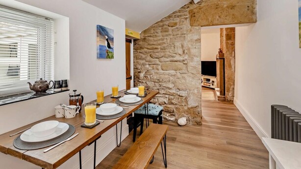A dining area with a stone wall, wooden table, and benches. - 2 Bed in Morpeth (oc-91206) (Amble)