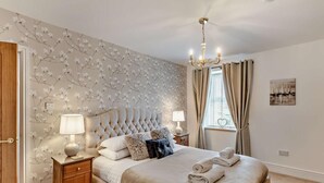 A bedroom with a tufted headboard, two bedside tables with lamps, a window with curtains, and a painting on the wall. - 2 Bed in Morpeth (oc-91206) (Amble)