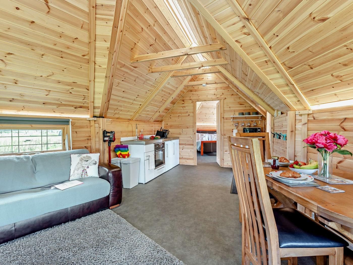 A cozy wooden cabin interior with a dining area, kitchen, and a living room with a sofa.