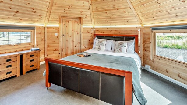 A wooden cabin bedroom with a bed, a dresser, and a window.