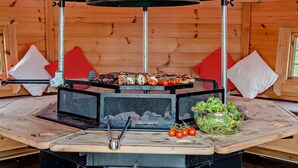 A wood-paneled room with a grill station featuring a black grill hood, a metal grill, and a variety of food items.