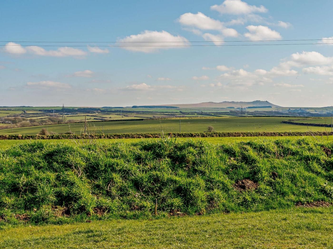 A rural landscape with rolling hills, a clear sky, and a distant hill.