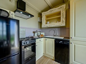 A kitchen with a black refrigerator, stove, oven, and dishwasher. There is a white cabinet with a decorative frame above the sink. - 1 Bed in Camelford (oc-90818) (Forrabury and Minster)