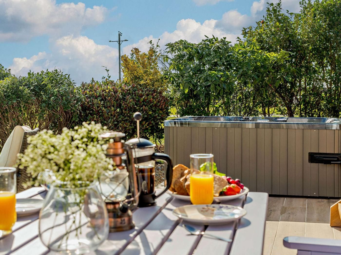 An outdoor dining area with a table set for breakfast, including a coffee pot, a glass of orange juice, and plates of food.
