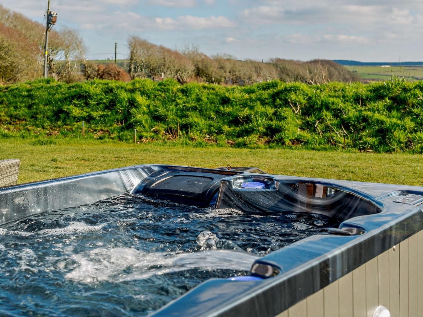 A hot tub outdoors with a grassy area and trees in the background.