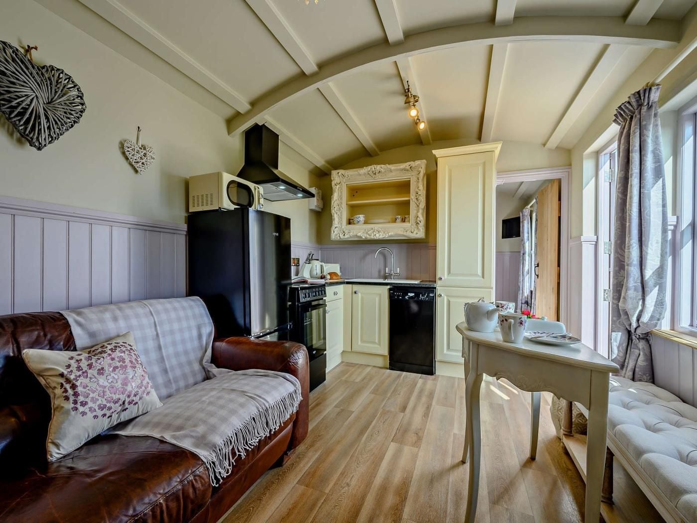 A cozy living area with a brown leather sofa, a small table, and a kitchen with a microwave, oven, and sink.