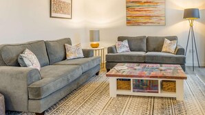 A modern living room with two grey sofas, a coffee table with a colorful top, a floor lamp, and two wall art pieces. - 3 Bed in Rye- (oc-90766) (Rye)