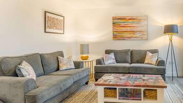 A modern living room with two grey sofas, a coffee table with a colorful top, a floor lamp, and two wall art pieces.