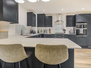 A modern kitchen with dark cabinets, a central island, and a stainless steel range hood. - 3 Bed in Rye- (oc-90766) (Rye)