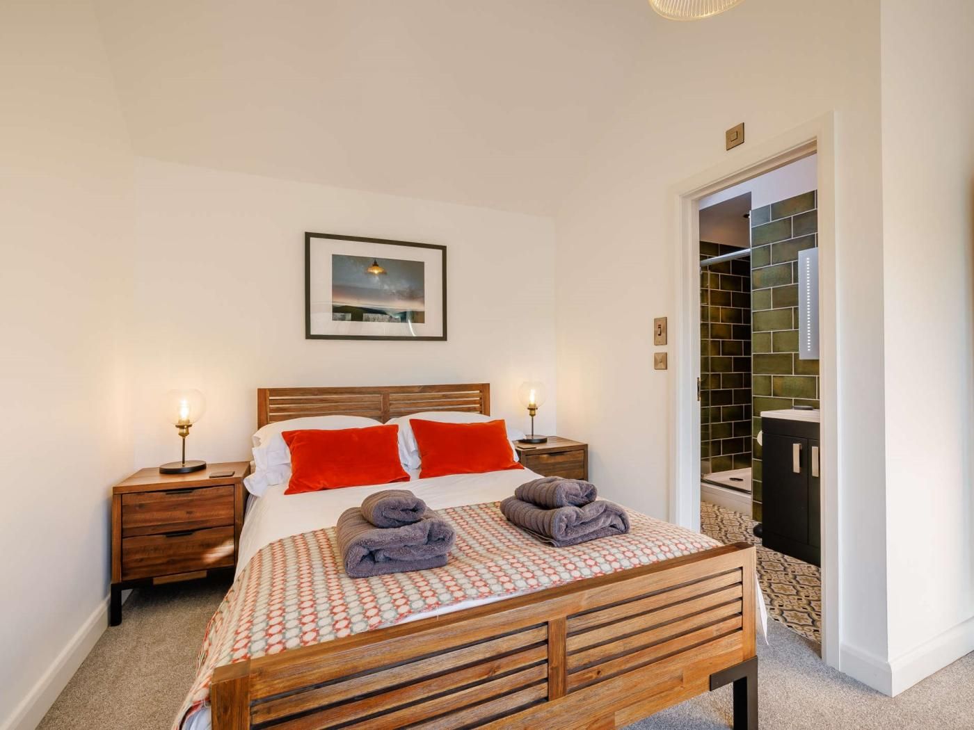 Een hotelkamer met een houten bed, twee nachtkastjes met lampen, een lijst aan de muur en uitzicht op de badkamer door een geopende deur.