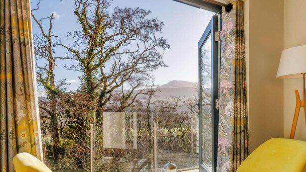 Habitació amb dues cadires grogues, una taula petita amb una tetera i tasses, i vista a arbres i muntanyes.