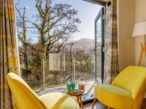 A room with two yellow chairs, a small table with a teapot and cups, and a view of trees and mountains. - 3 Bed in Dolgellau (oc-90805) (Llanelltyd)