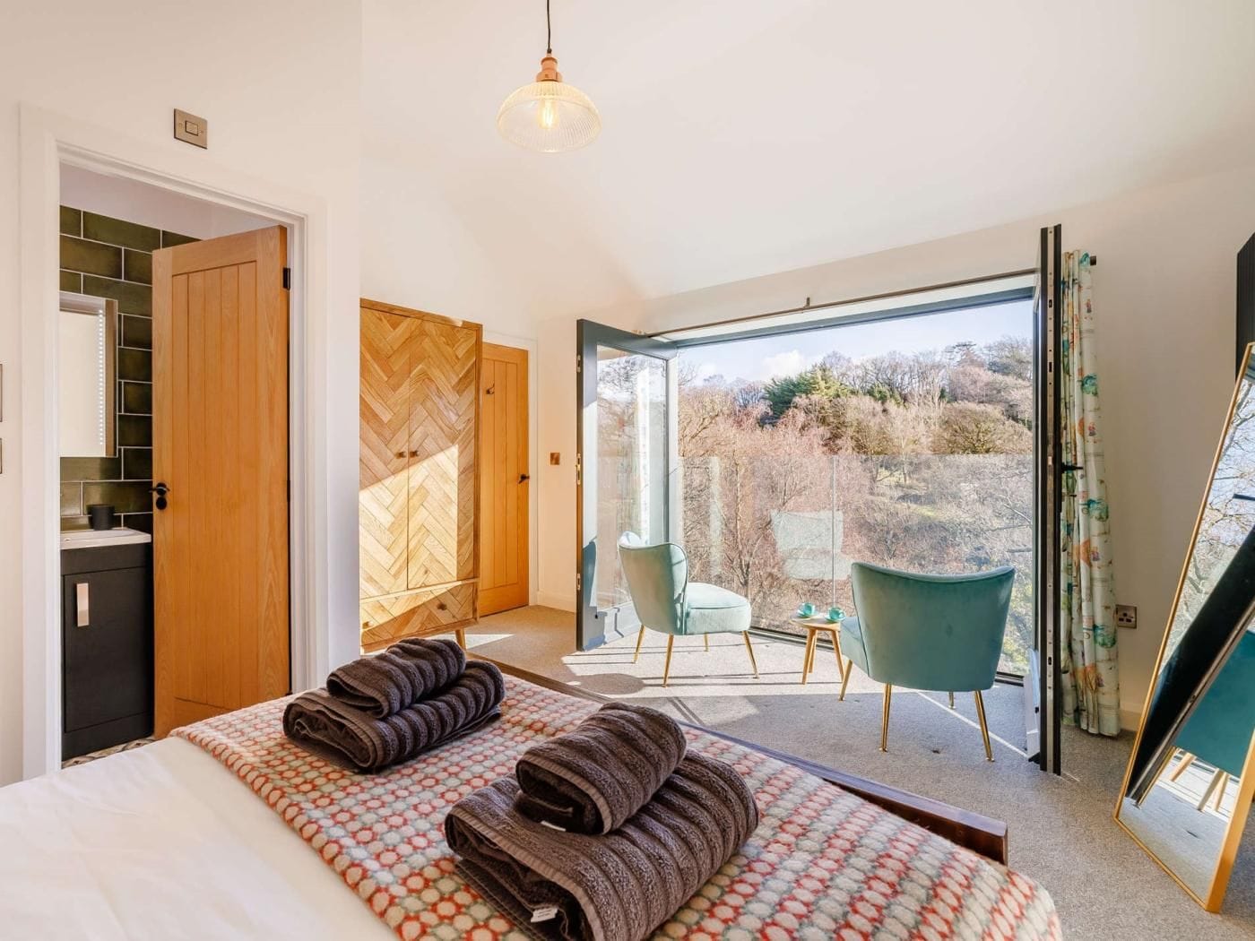 A bedroom with a large bed, a wooden wardrobe, a bathroom, and a balcony with chairs.