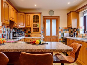 Una cocina con armarios de madera, encimera de granito, comedor con sillas de cuero y salpicadero de azulejos.