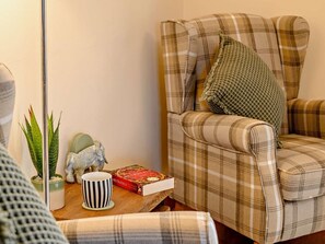 Un sillón de cuadros con un cojín, una mesita con una planta, una taza y un libro.