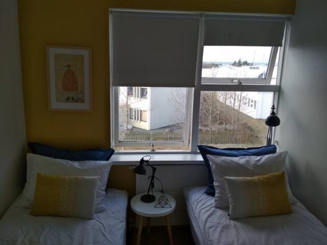 Une chambre avec deux lits, une fenêtre, une petite table et une lampe.