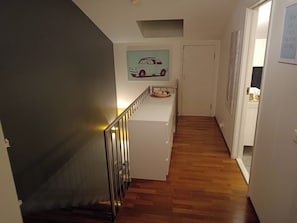 A hallway with a staircase, a wall-mounted artwork of a car, and a door leading to another room. - Charming 2-bedroom apartment in Seltjarnarnes (Seltjarnarnes)