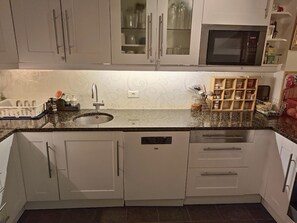 A kitchen with white cabinets, a granite countertop, a built-in microwave, and a dish rack. - Charming 2-bedroom apartment in Seltjarnarnes (Seltjarnarnes)