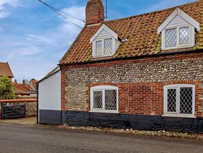 A stone house with a tiled roof, two windows with white frames and diamond-patterned glass, and a chimney. - 3 Bed in Holt (oc-90943) (Weybourne)