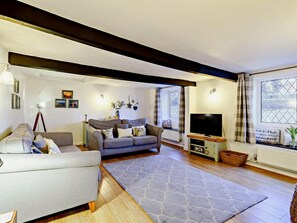 Ein Wohnzimmer mit einer Couch, einem Fernseher, einem Fenster mit Vorhängen und einer Wand mit gerahmten Bildern.