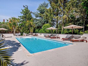 Ein rechteckiger Pool mit Liegestühlen und Sonnenschirmen, umgeben von Bäumen und einer weißen Mauer.
