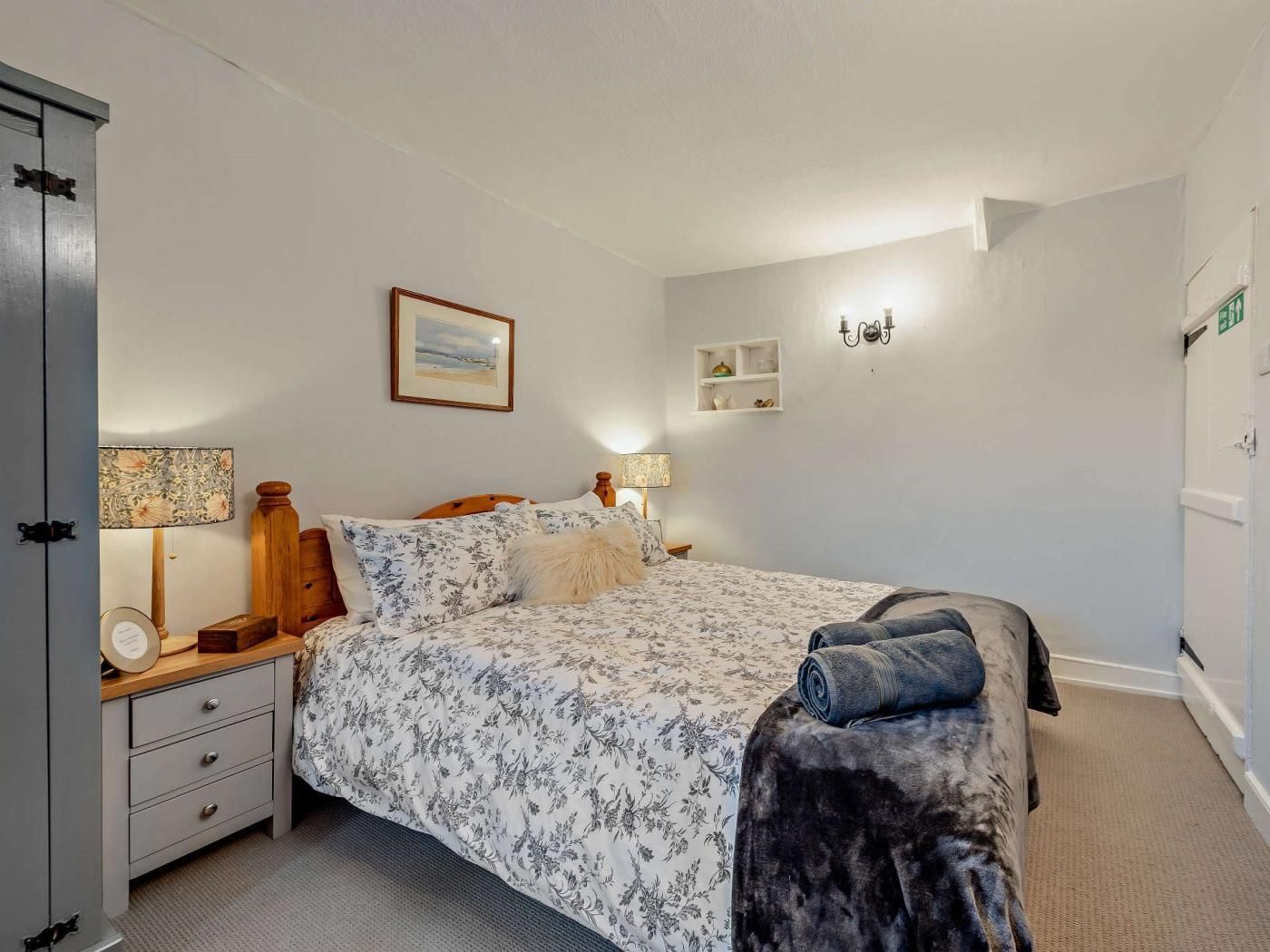 Une chambre à coucher avec un lit, des tables de chevet, une lampe, un tableau encadré au mur et une armoire.