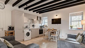 A modern kitchen with a washing machine, dining area with chairs, and a grey sofa. - 3 Bed in Crieff (oc-90794) (Comrie)