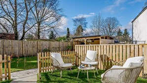A backyard with a wooden fence, a paved walkway, and outdoor furniture including wicker chairs and a table. - 3 Bed in Crieff (oc-90794) (Comrie)