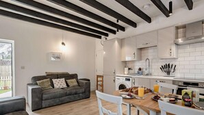 A modern kitchen with white cabinets, a dining table with chairs, a grey sofa, and a washing machine. - 3 Bed in Crieff (oc-90794) (Comrie)
