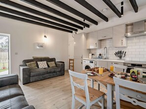 A modern kitchen with white cabinets, a dining table with chairs, a grey sofa, and a washing machine. - 3 Bed in Crieff (oc-90794) (Comrie)