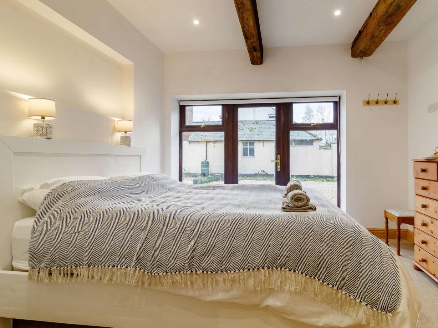 A bedroom with a bed, bedside lamps, a window, and a wooden dresser.