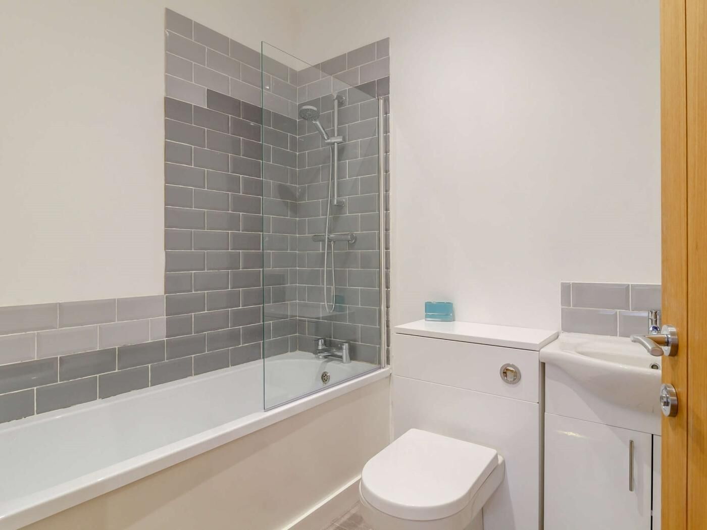 A bathroom with a glass-enclosed shower, a white toilet, and a sink with a wooden door.
