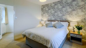 Une chambre à coucher avec un lit, deux lampes de chevet, une table de chevet ornée d’un vase et un mur décoré d’un motif floral.