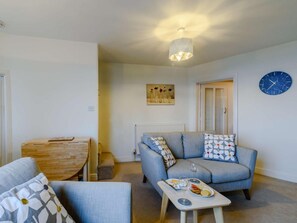 Ein Wohnzimmer mit einer Couch, einem Couchtisch mit Speisen und Getränken, einem Esstisch und einer Deckenleuchte.