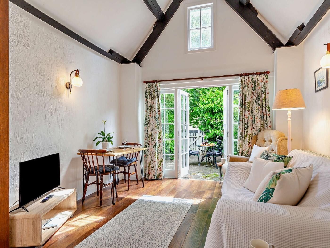 A room with a TV, wooden dining table, chairs, a sofa, and a large window with curtains.