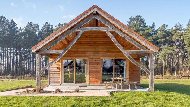 A wooden cabin with a pitched roof, large glass windows, and a picnic table outside. - 2 Bed in King's Lynn (oc-91275) (North Runcton)