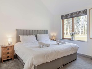 Um quarto com cama, mesas de cabeceira, janela com vista para árvores e uma luminária.