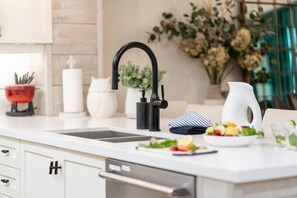 Eine moderne Küche mit einem schwarzen Wasserhahn, einer weißen Spüle, einem roten Topf, einem weißen Krug und einer Schüssel mit Obst auf der Arbeitsplatte.