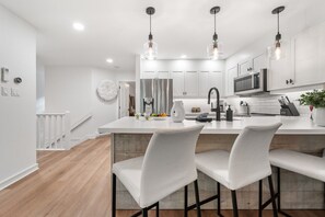 A modern kitchen with white cabinetry, a central island with bar stools, pendant lighting, and a stainless steel range hood. - Near Gondola & Lake | Private Hot Tub| Free Ski Shuttle & Parking (Whistler)
